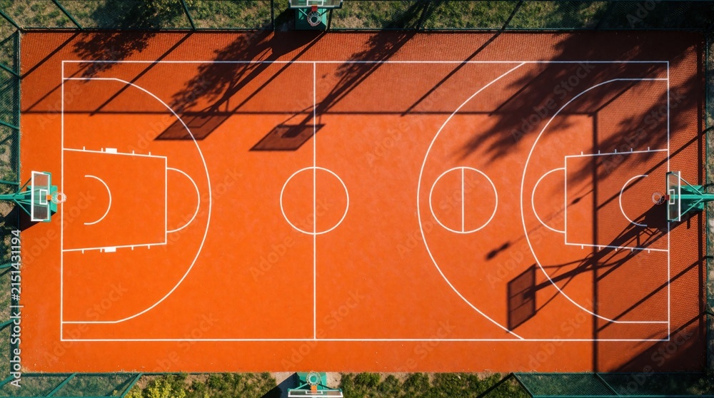 Fototapeta premium Aerial view of bright orange basketball court with white lines. Outdoor sports field from above in sunlight. Shadows cast on the empty playground.