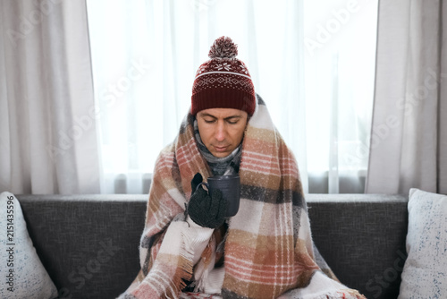 Fotografie Freezing man wrapped in a blanket holds a warm mug at home