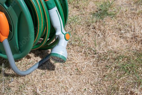 Konstfotografi Dried-up, sunburnt grass which has turned yellow from a lack of water, with green hose pipe with grey watering nozzle laying on the ground