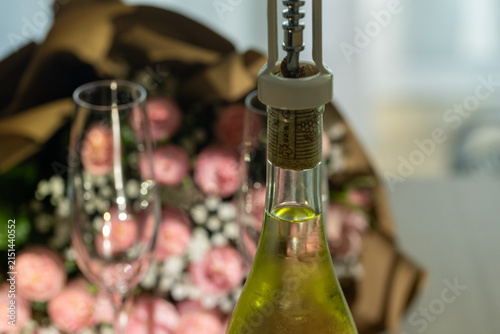 Foto Pop open a bottle of sparkling drink with flowers and glasses in the background