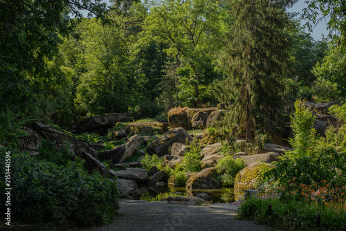 Picturesque rocky landscape with moss-covered granite boulders, lush vegetation and a small stream in Sofiyivka National Dendrological Park in Uman, Ukraine.