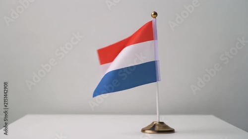 Small Netherlands Flag Waving on White Table Desk Stand Isolated on Grey Background