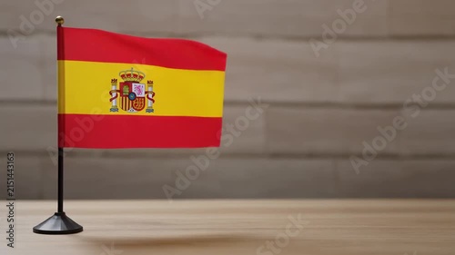 Small Spain Flag Waving on Wooden Table Desk Stand Isolated on Light Wall Background