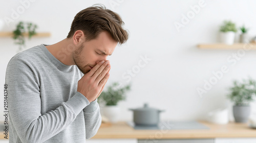 Contemplative Caucasian man in a gray sweater feeling stressed in a bright kitchen.
