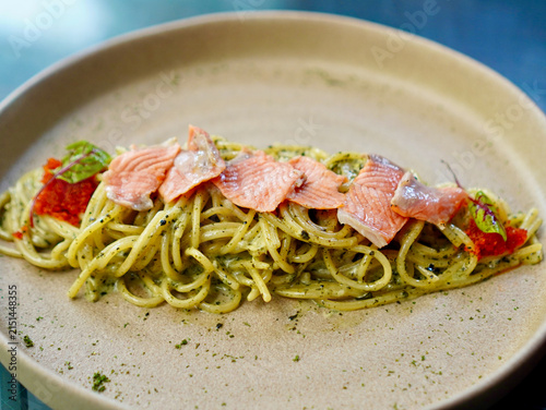 Creamy green seaweed carbonara spaghetti garnished with salmon fillets and fresh microgreens on a modern plate