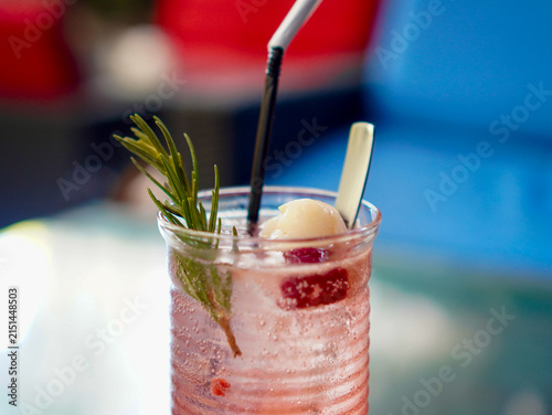 Cold fruity soda beverage with lychee fruit, raspberries, and rosemary sprig served outdoors in a tall glass