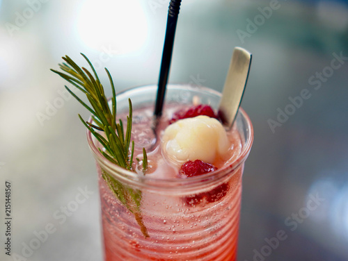 Refreshing pink lychee berry soda cocktail with ice cubes, fresh rosemary garnish, and black straw in a tall glass