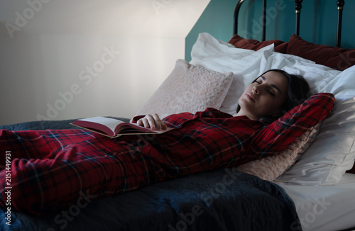 Tired woman sleeping with an open book in bed