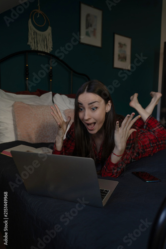 Obraz na płótnie Surprised woman reacting to laptop while lying on bed