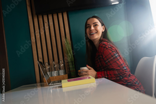Happy woman enjoying coffee break beside laptop at home
