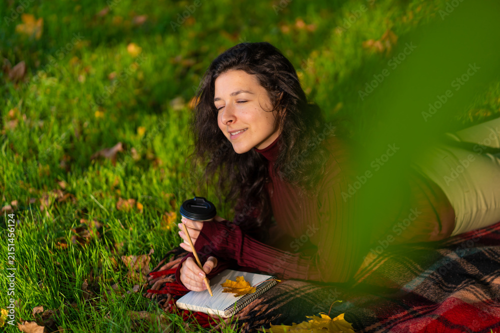 Obraz premium Person writes notes lying on the lawn in the autumn park. Solitude with yourself