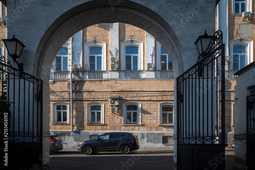 Moscow, Russia, through a historic arched gateway with wrought-iron gates onto a street where a dark SUV is parked.
