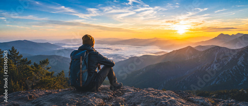 Hiker sits atop mountain watching sunrise over valleys