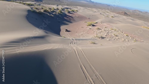 Dynamic aerial FPV view of off road 4WD vehicle driving through sand dunes landscape