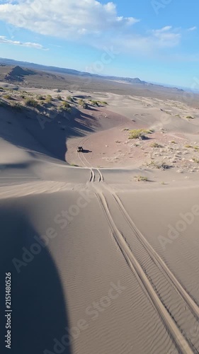 Vertical FPV drone shot flying over desert sand dunes revealing 4x4 vehicle