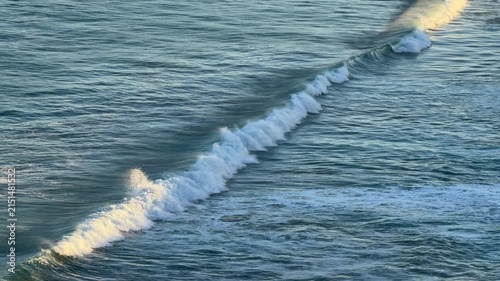 Tracking shot over blue ocean waves building and breaking in later afternoon light in 4k footage