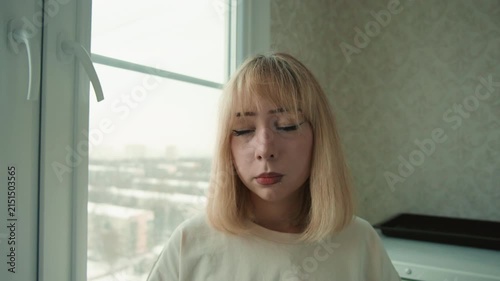 Woman tasting lemon near window, grimace and thumbs down, cooking taste test, home kitchen ambiance, candid vlogstyle frame, cold winter cityscape outside, natural soft light, unsatisfied flavor