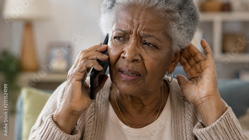 Frustrated senior African American woman talking on smartphone, holding hand to ear, straining to hear. Annoyed elderly Black lady having hearing problems, bad connection, or dementia confusion concep