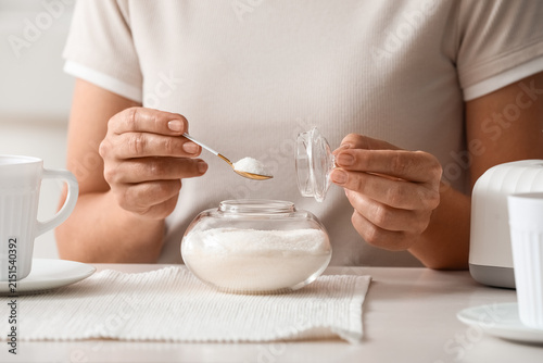 Bild auf Leinwand Womans hands adding white sugar from a glass bowl with a small spoon to a bevera