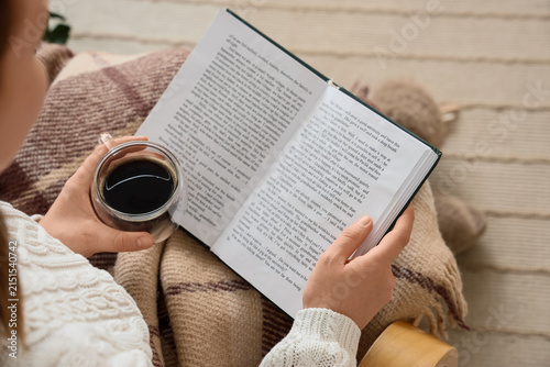 Woman reading a book and drinking coffee, cozy autumn morning at home, relaxa...