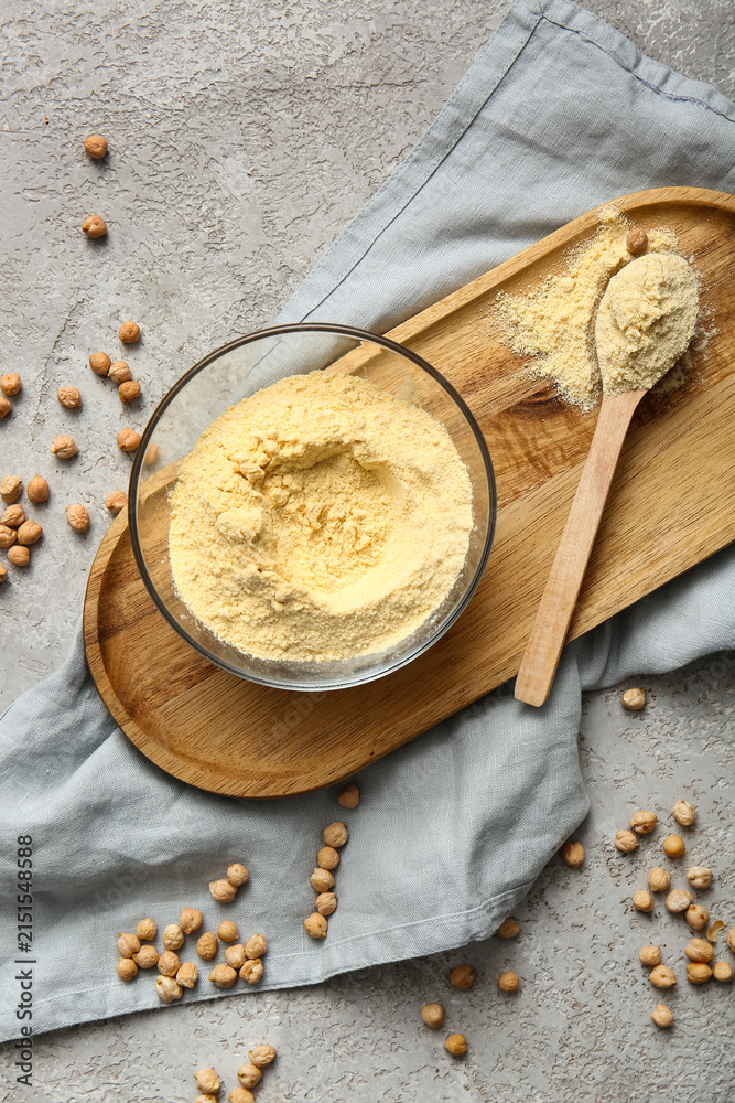 Fototapeta premium Glass bowl and wooden spoon with chickpea flour on grey background