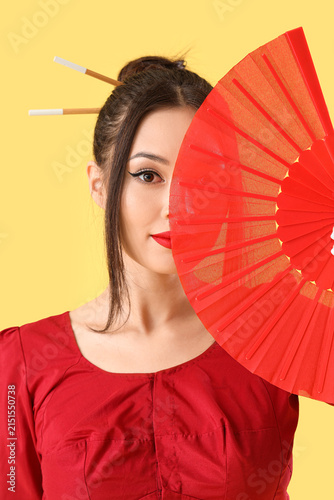Young Asian woman with fan on yellow background, closeup. Chinese New Year ce...