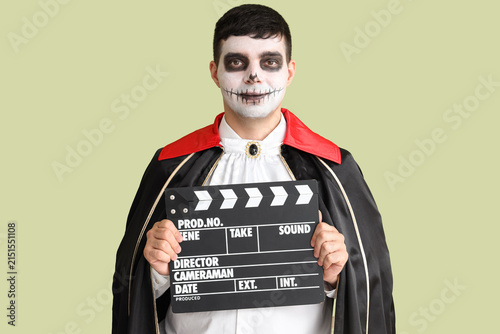 Handsome young man dressed for Halloween as vampire with clapperboard on gree...