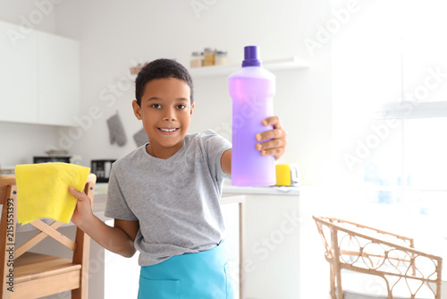 Cute little African-American boy with cleaning supplies in kitchen