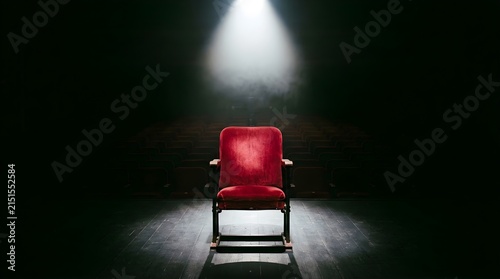 Empty red velvet theater seat illuminated by a single spotlight on stage