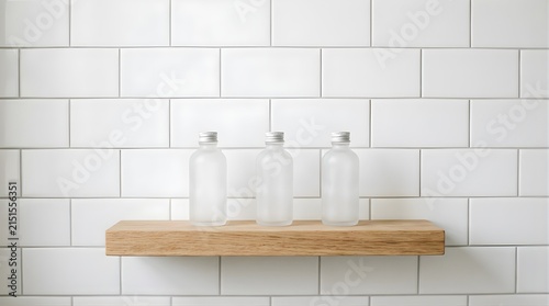 Three frosted glass cosmetic bottles on a wooden shelf against white tiles