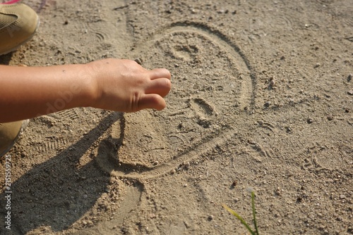 Close-up of a child drawing pictures in the sand on the ground with hand