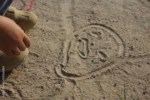 Drawing of a face in the sand on the ground and a child's hand