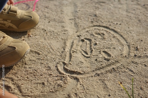 Drawing of a face in the sand on the ground and a child's hand