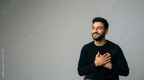 Smiling man holding hands on chest, expressing gratitude and heartfelt emotion, ideal for wellness, mental health and appreciation campaigns.