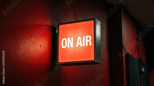 A glowing red rectangular sign with the text on air in white letters is mounted on a dark red wall in a broadcast or recording studio space
