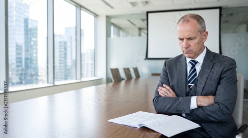 Serious mature businessman sitting in conference room reviewing contract