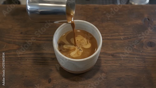 Barista pouring coffee and milk into a ceramic cup on a wooden table
