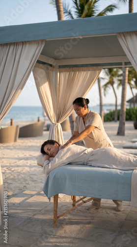 Woman receiving back massage inside a white curtained beach cabana