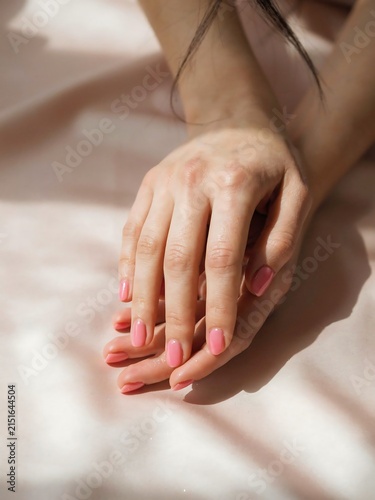 Female Hands with Pink Nails Resting on Soft Pink Fabric with Shadows, Close-up