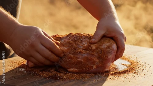 Close-Up Of Applying Savory Spice Rub On Pork Shoulder In Warm Outdoor Setting With Sunlight And Natural Background