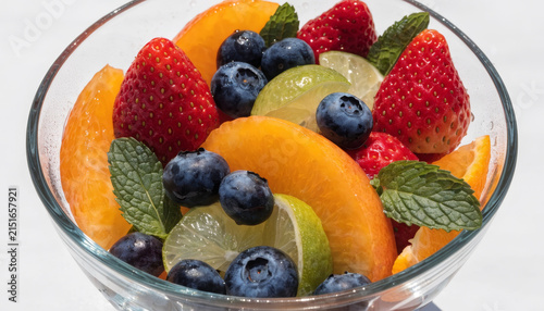 Fresh fruit salad with orange slice, strawberry, blueberry, lime slice, and mint leaf in glass bowl, vibrant and healthy, perfect for summer refreshment