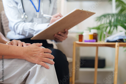 Close up of senior patient hands resting while doctor takes notes on clipboard during consultation