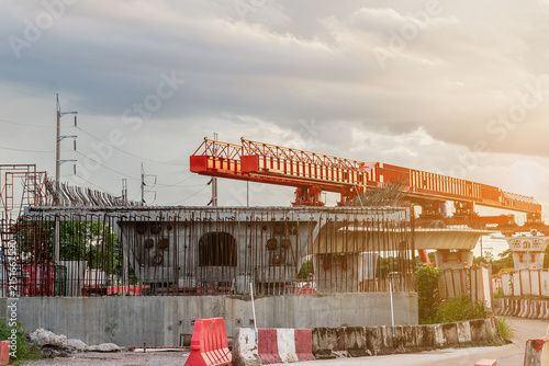 Image shows a construction site for a new concrete road and bridge, with large red steel beams and cranes at work a crucial infrastructure project for a major city.