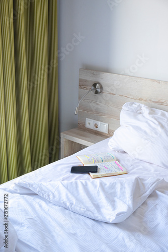 A smart phone and a note book on a neatly made hotel bed, symbolizing a peaceful morning routine.