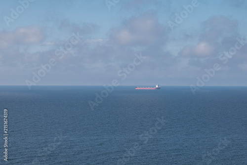 a cargo ship sailing in the distance on a calm sea under a cloudy sky