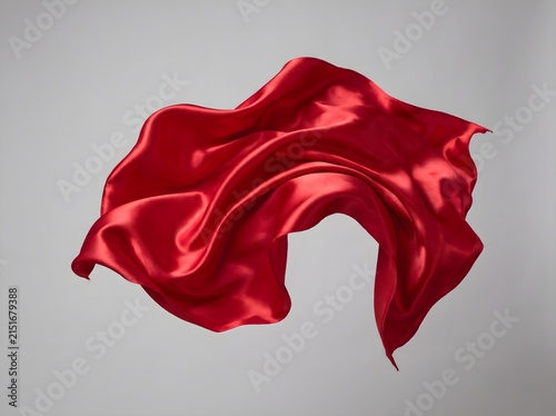 A piece of red silk fabric floating in the air against a neutral grey studio background