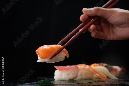 Image of a hand holding chopsticks and picking up sushi sashimi. Traditional Japanese culinary concept.