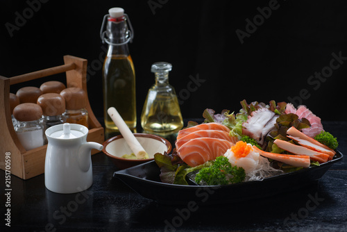 A sashimi set includes salmon, shrimp, octopus, and various sauces and seasonings, beautifully arranged on the table, a traditional Japanese culinary concept.