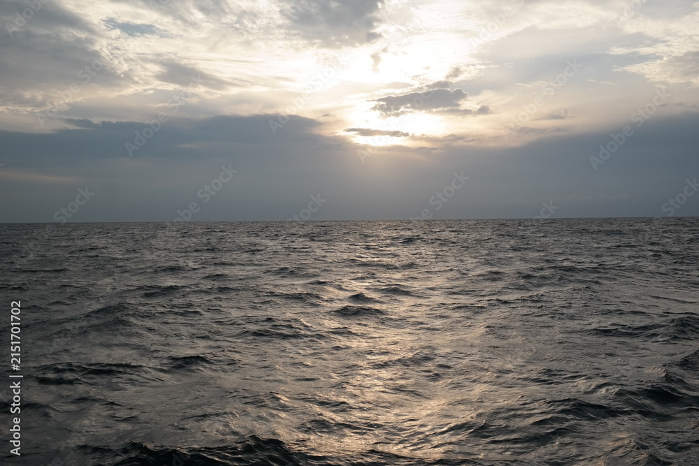 Obraz premium Golden Sunlight Over a Calm Ocean Horizon Beneath Dramatic Clouds