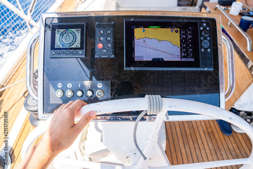Hand steering a modern sailing yacht using GPS chartplotter and navigation instruments. Marine navigation technology supporting safe offshore sailing and vessel control.